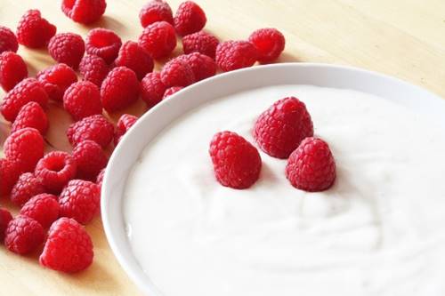 bowl with yogurt and some raspberries in it and around it