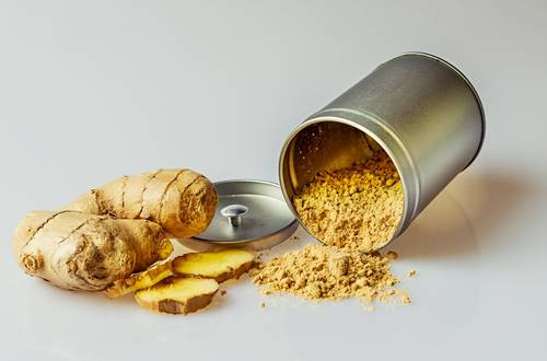 ginger root, sliced and ginger powder in a can and on a white surface