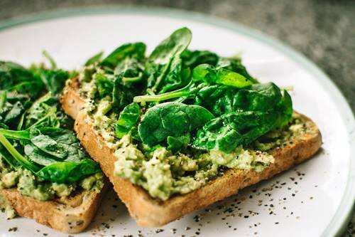 arugula leaves topping two slices of toast with cream cheese spread and pepper