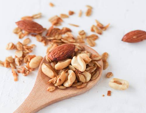 almonds, peanuts and rolled oats on a wooden spoon