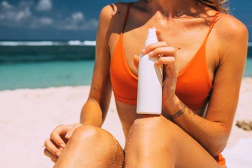 woman in orange bikini with sunscreen in a white bottle