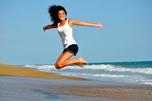 yong woman jumping in the air smiling on a beach by the sea, waves behind her